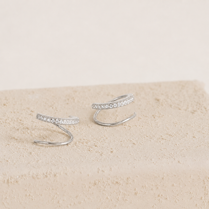 Silver ear cuffs with small stones on a beige surface