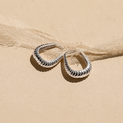 Silver hoop earrings on a sandy surface