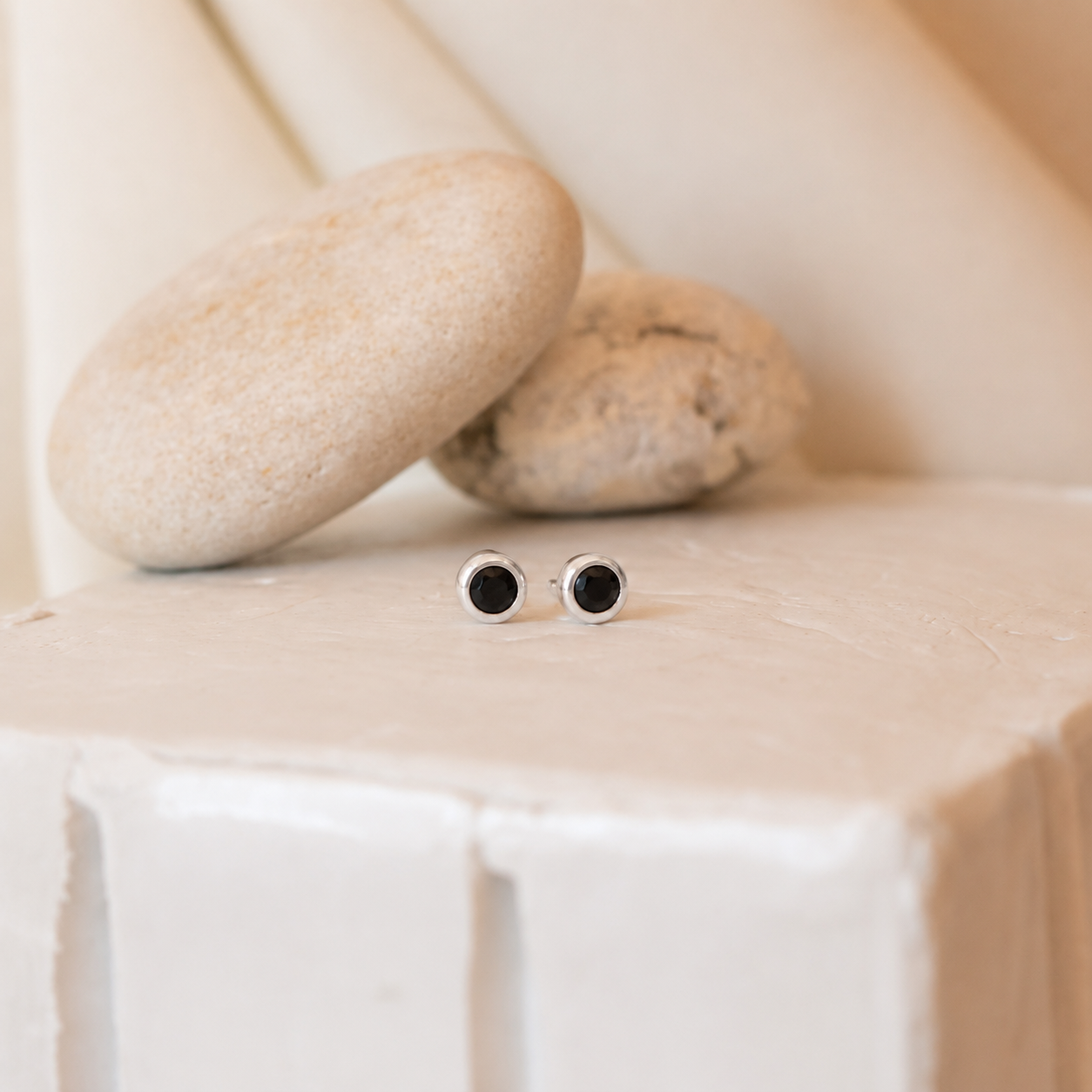 Pair of black and silver earrings on a white surface with stones in the background