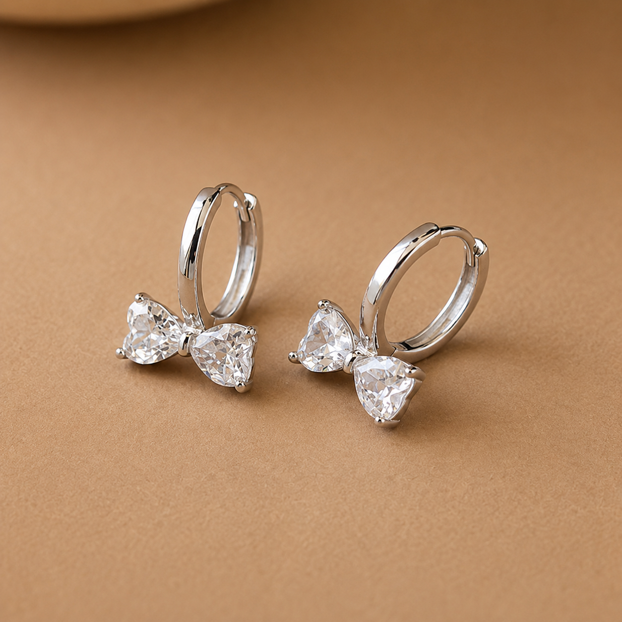 Silver bow-shaped earrings with clear gemstones on a brown background