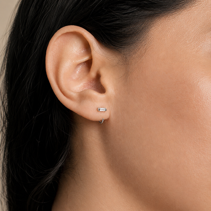 Close-up of an ear wearing a small earring with dark hair and skin background