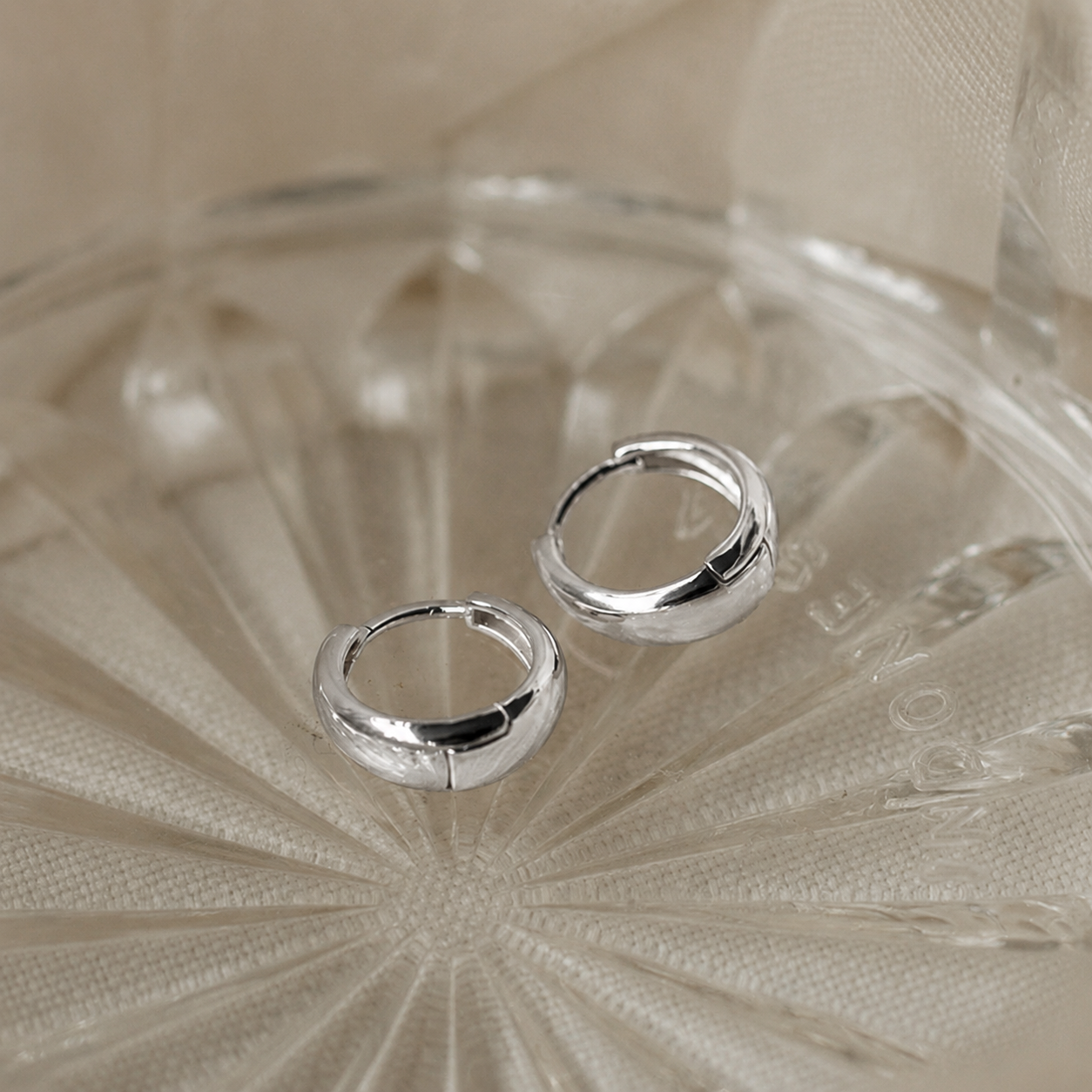 Silver hoop earrings on a textured beige surface