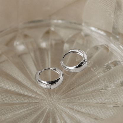 Silver hoop earrings on a textured beige surface
