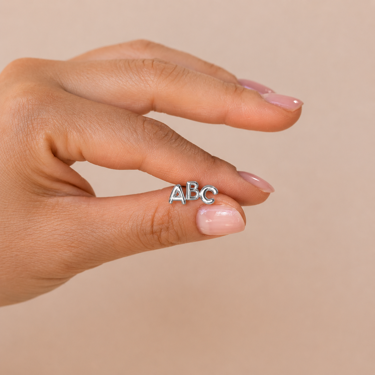 Hand wearing a silver 'ABC' ring on a beige background