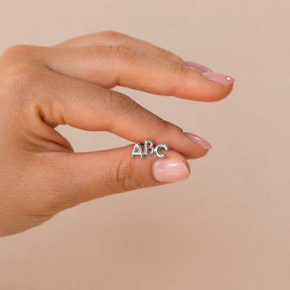 Hand wearing a silver 'ABC' ring on a beige background