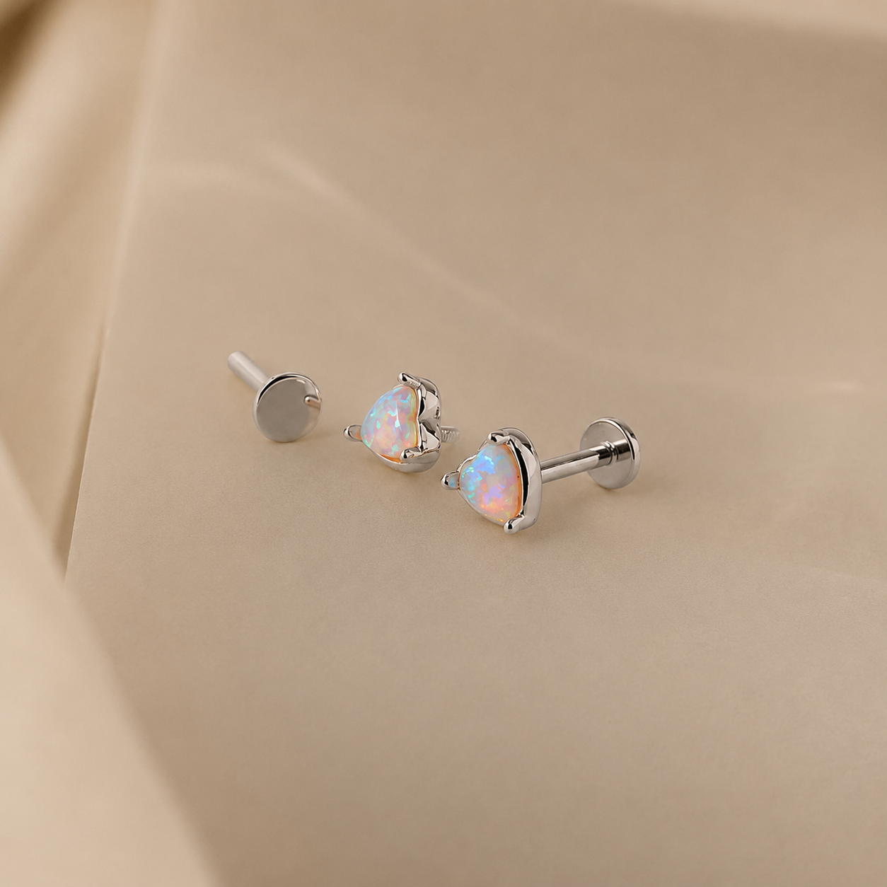 Pair of silver heart-shaped opal earrings on a beige fabric background