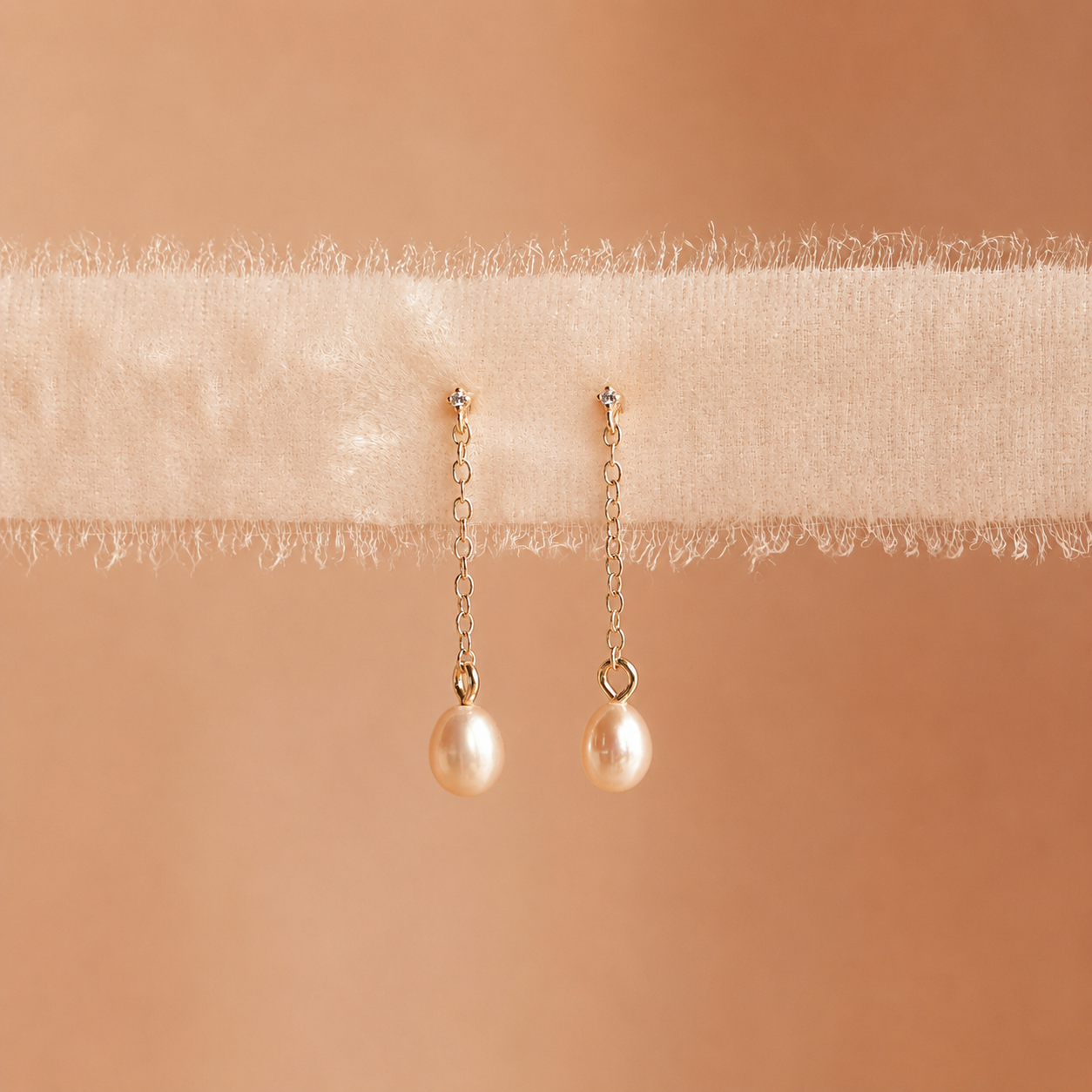 Pair of pearl earrings on a soft beige fabric background