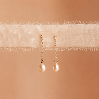 Pair of pearl earrings on a soft beige fabric background