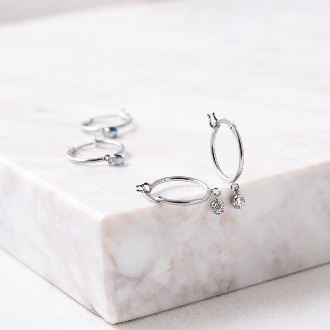 Silver hoop earrings with small gemstones on a marble surface