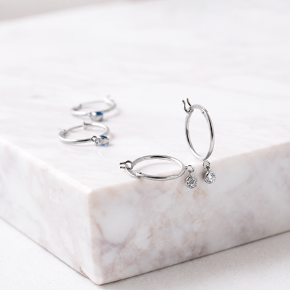 Silver hoop earrings with small gemstones on a marble surface