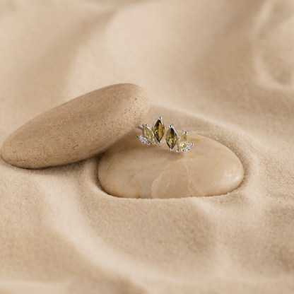 Silver earrings with green gemstones on a sandstone surface