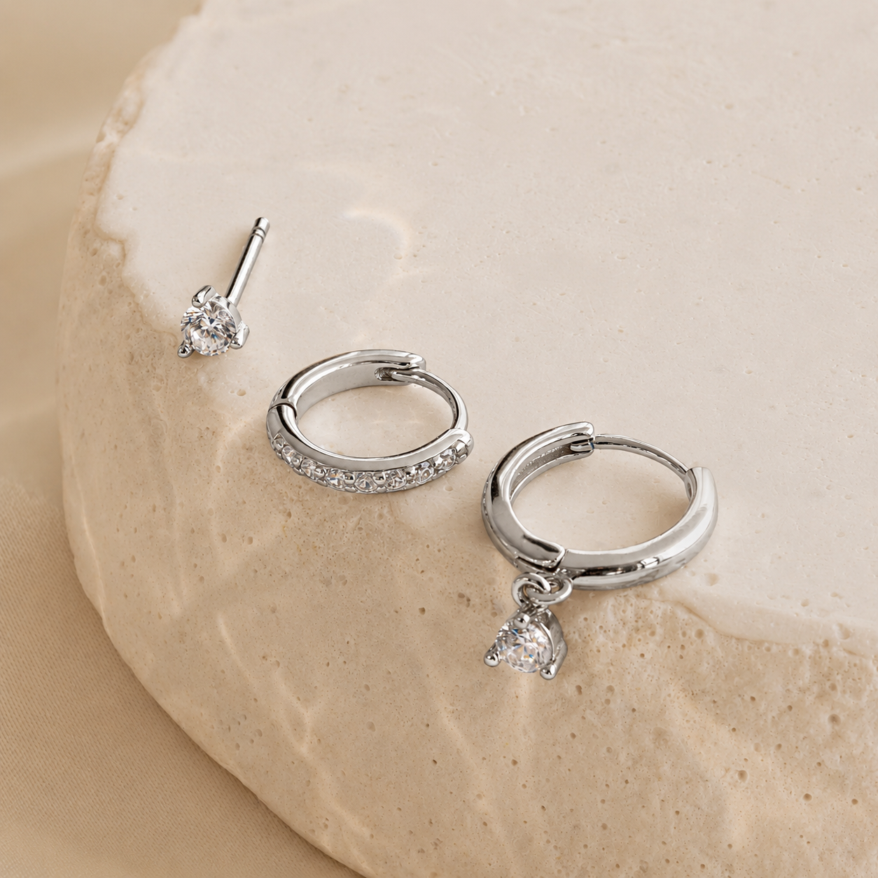 Silver hoop earrings with a small charm on a beige stone background