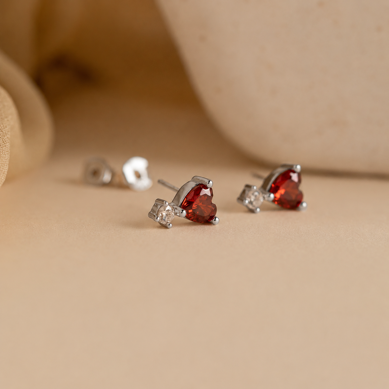 Heart-shaped red gemstone earrings on a beige background