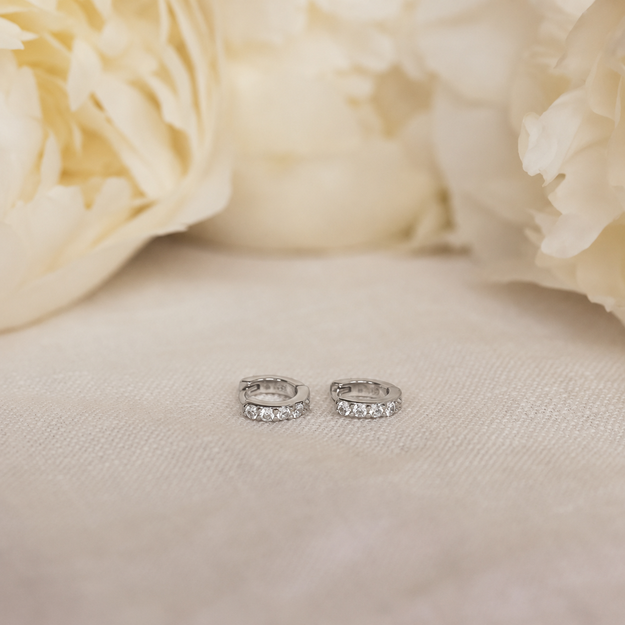 Silver hoop earrings on a beige fabric background with cream flowers