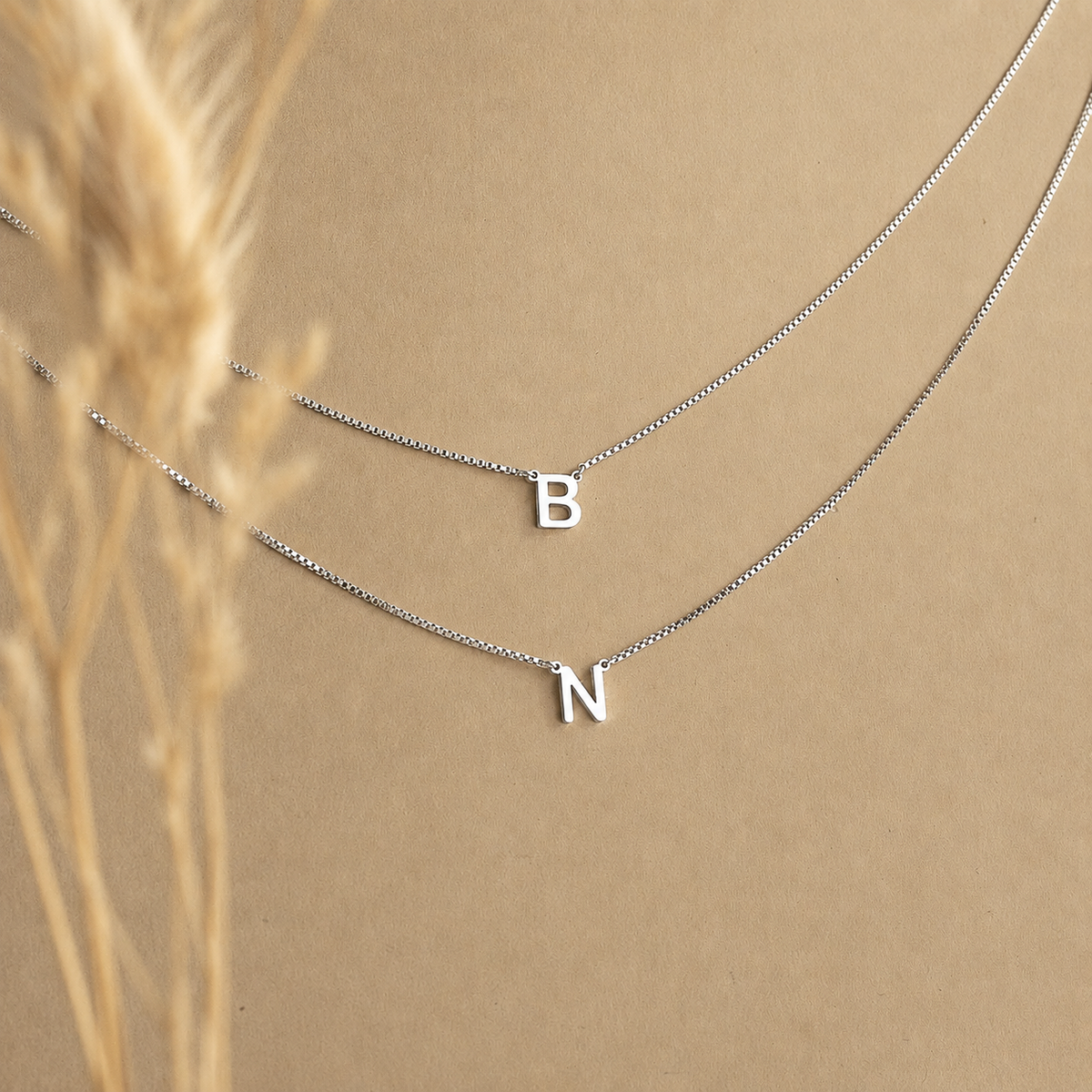 Silver necklace with letter 'B' and 'N' pendants on a beige background
