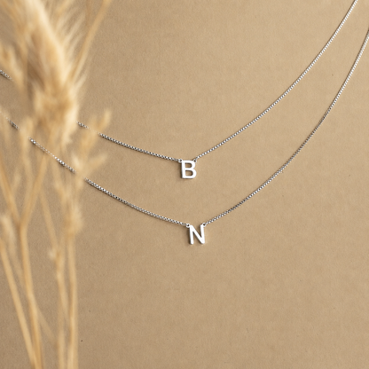 Silver necklace with letter 'B' and 'N' pendants on a beige background