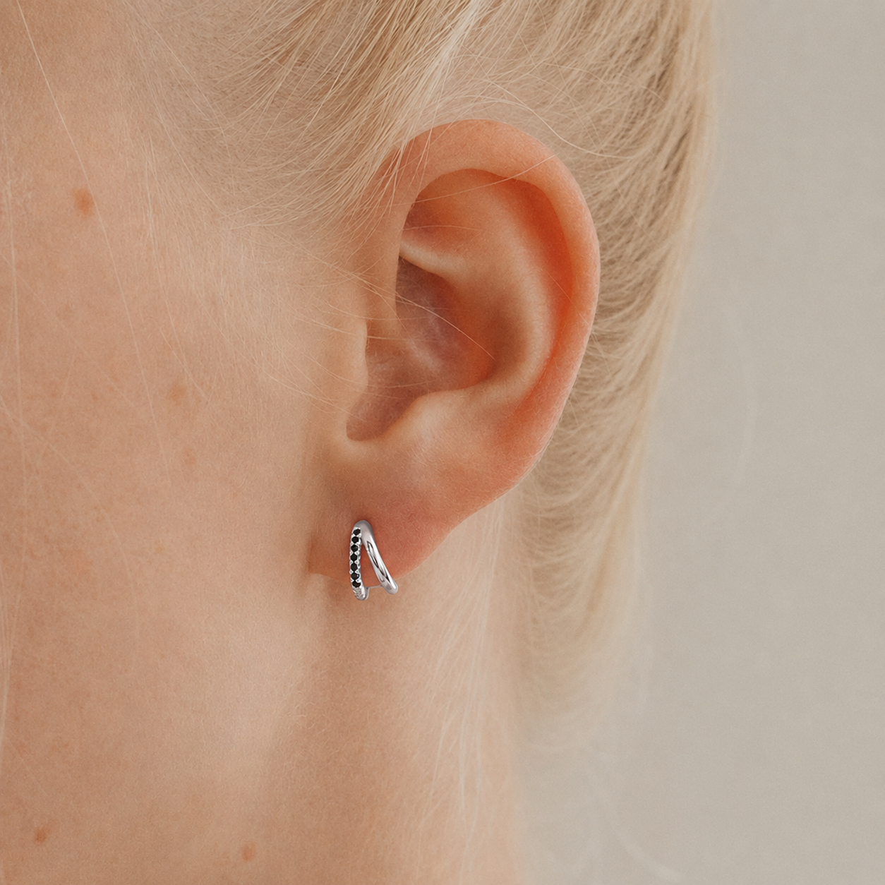 Close-up of an ear wearing a small silver earring with black stones on a neutral background