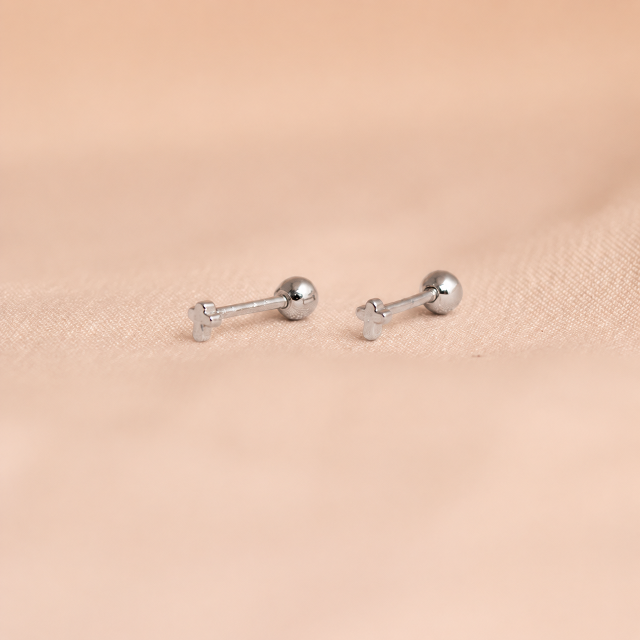 Pair of silver barbell-shaped earrings on a beige fabric background