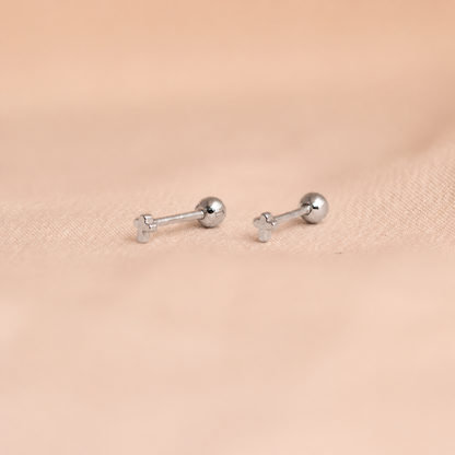 Pair of silver barbell-shaped earrings on a beige fabric background