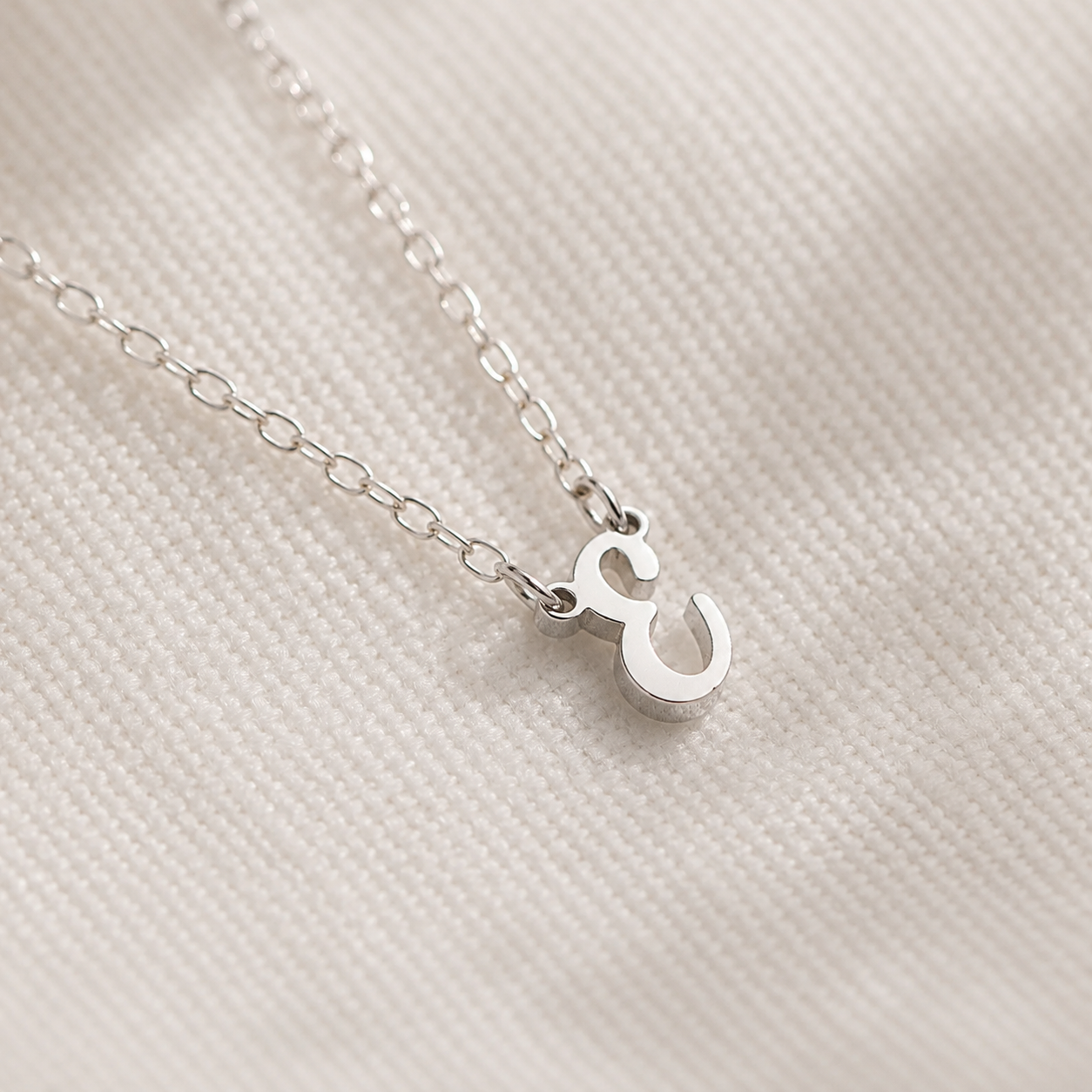 Silver necklace with a small pendant on a textured beige background
