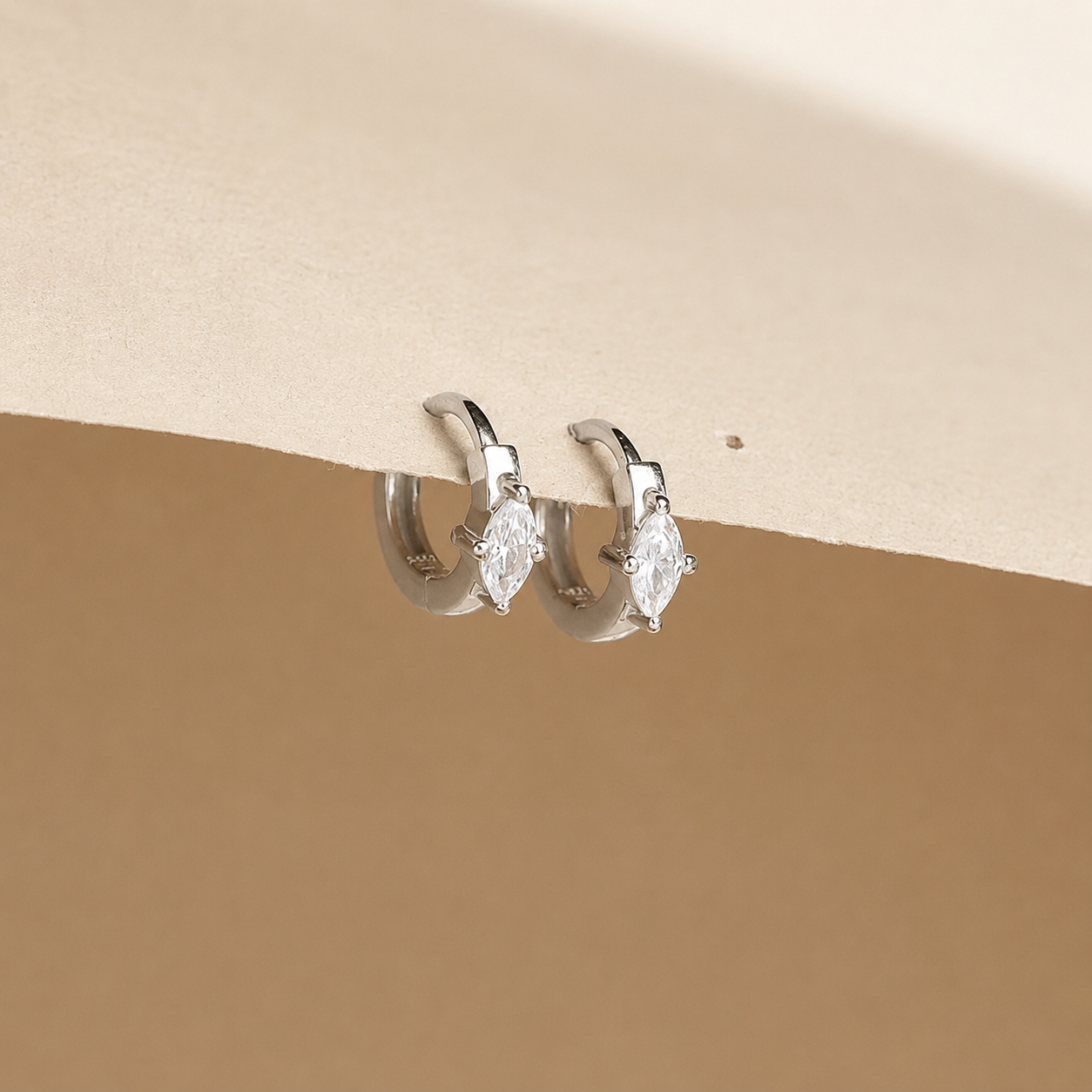 Pair of silver hoop earrings with clear gemstones on a beige background