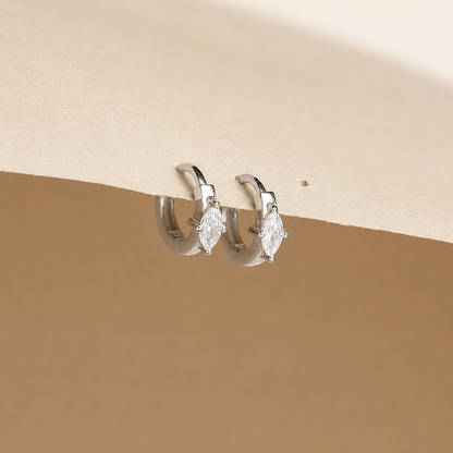 Pair of silver hoop earrings with clear gemstones on a beige background
