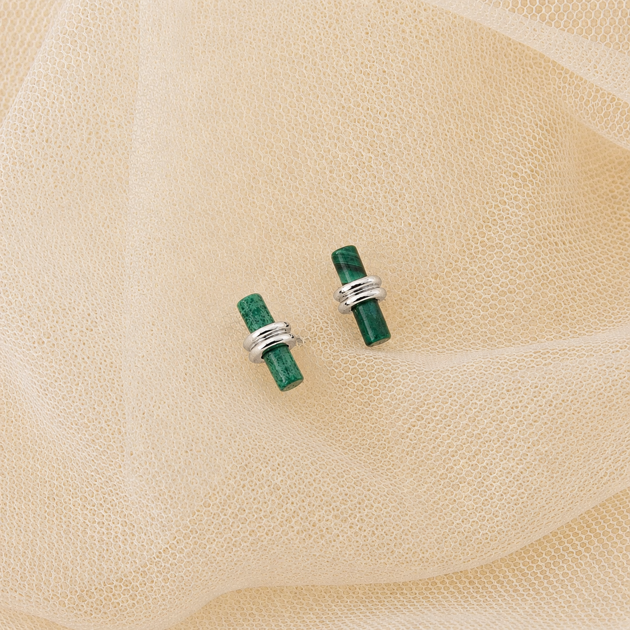 Green stone earrings with silver bands on a beige fabric background
