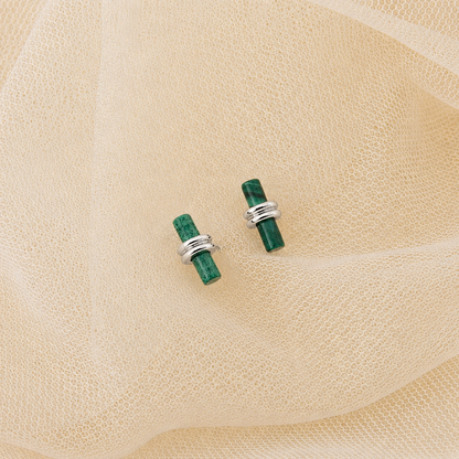 Green stone earrings with silver bands on a beige fabric background