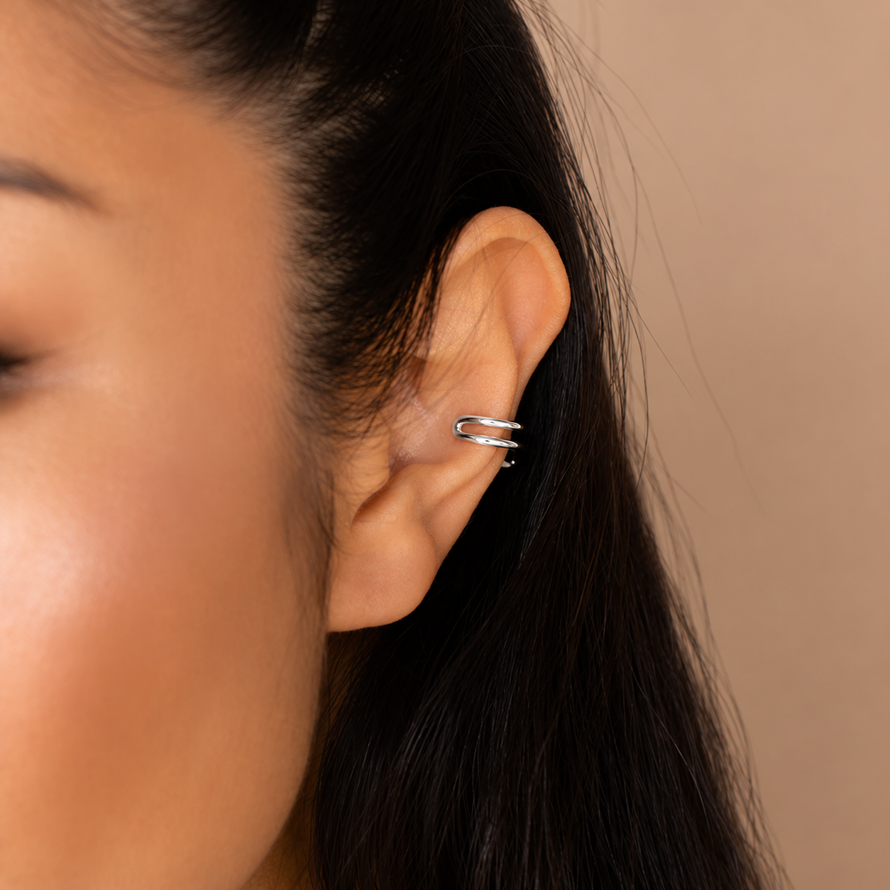 Close-up of an ear wearing a silver earring with a plain background