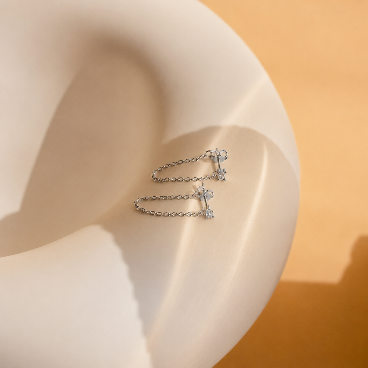 Silver chain earring with heart and star charms on a mannequin ear against an orange background