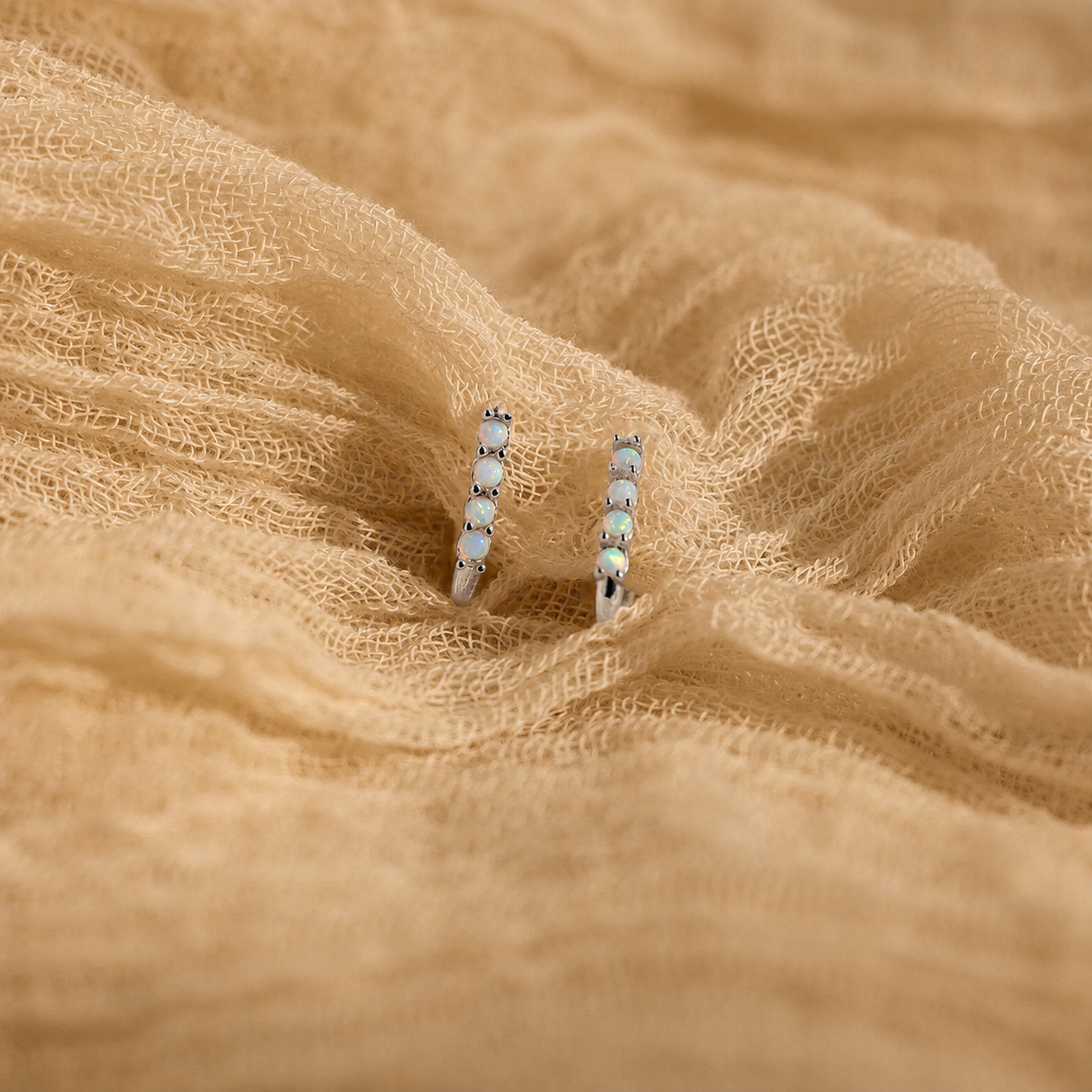 Pair of silver earrings with gemstones on a beige fabric background