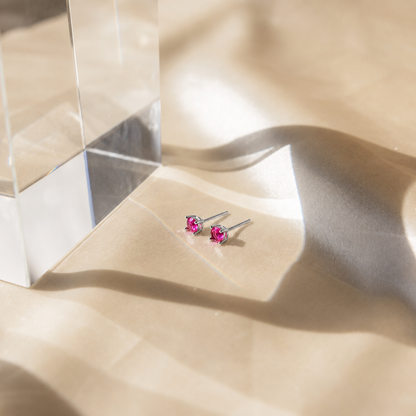Pink gemstone stud earrings on a beige fabric background