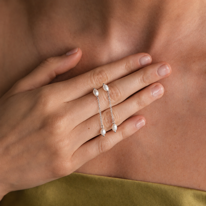 Hand wearing two silver rings with pearl-like stones on a neutral background
