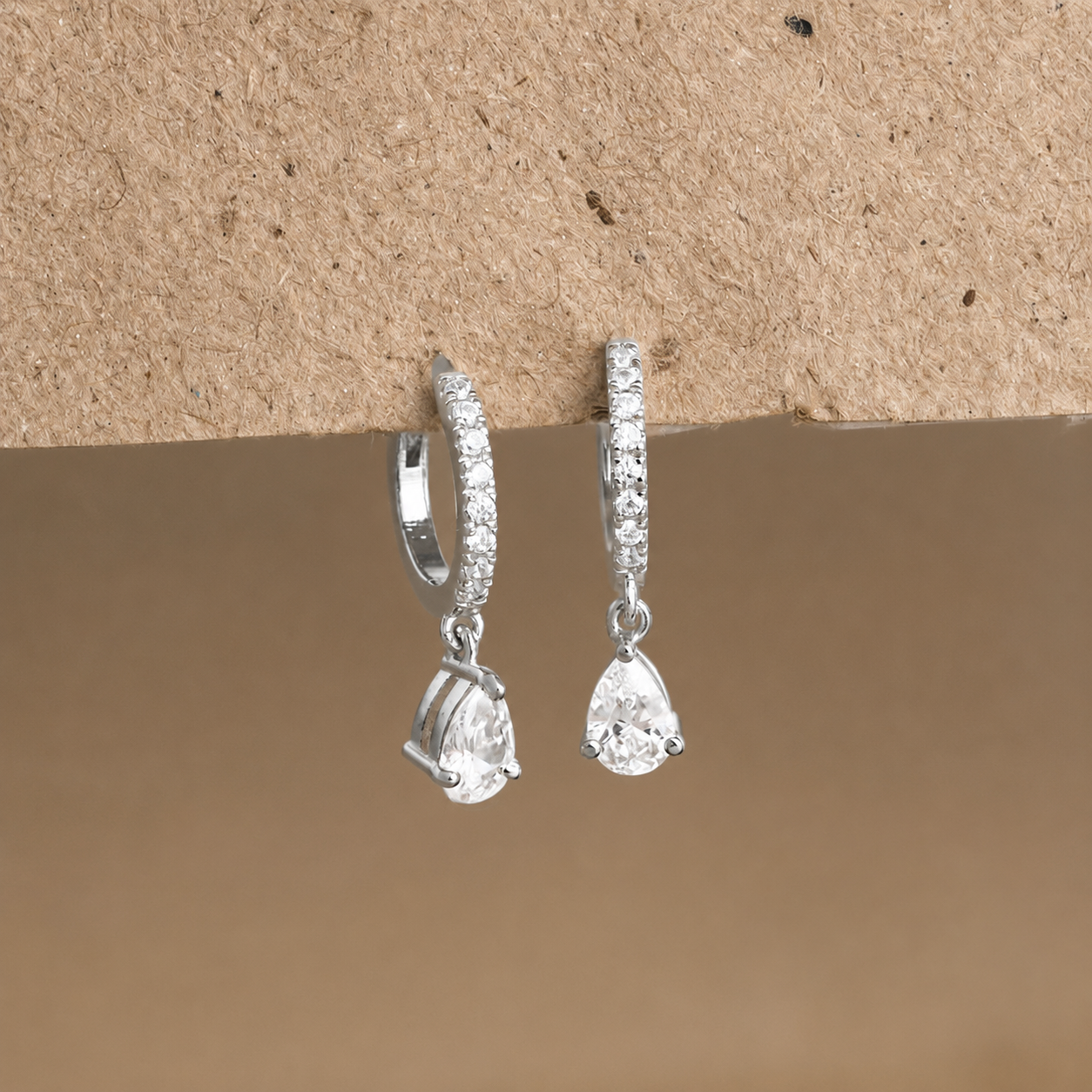 Pair of silver teardrop earrings on a textured brown surface