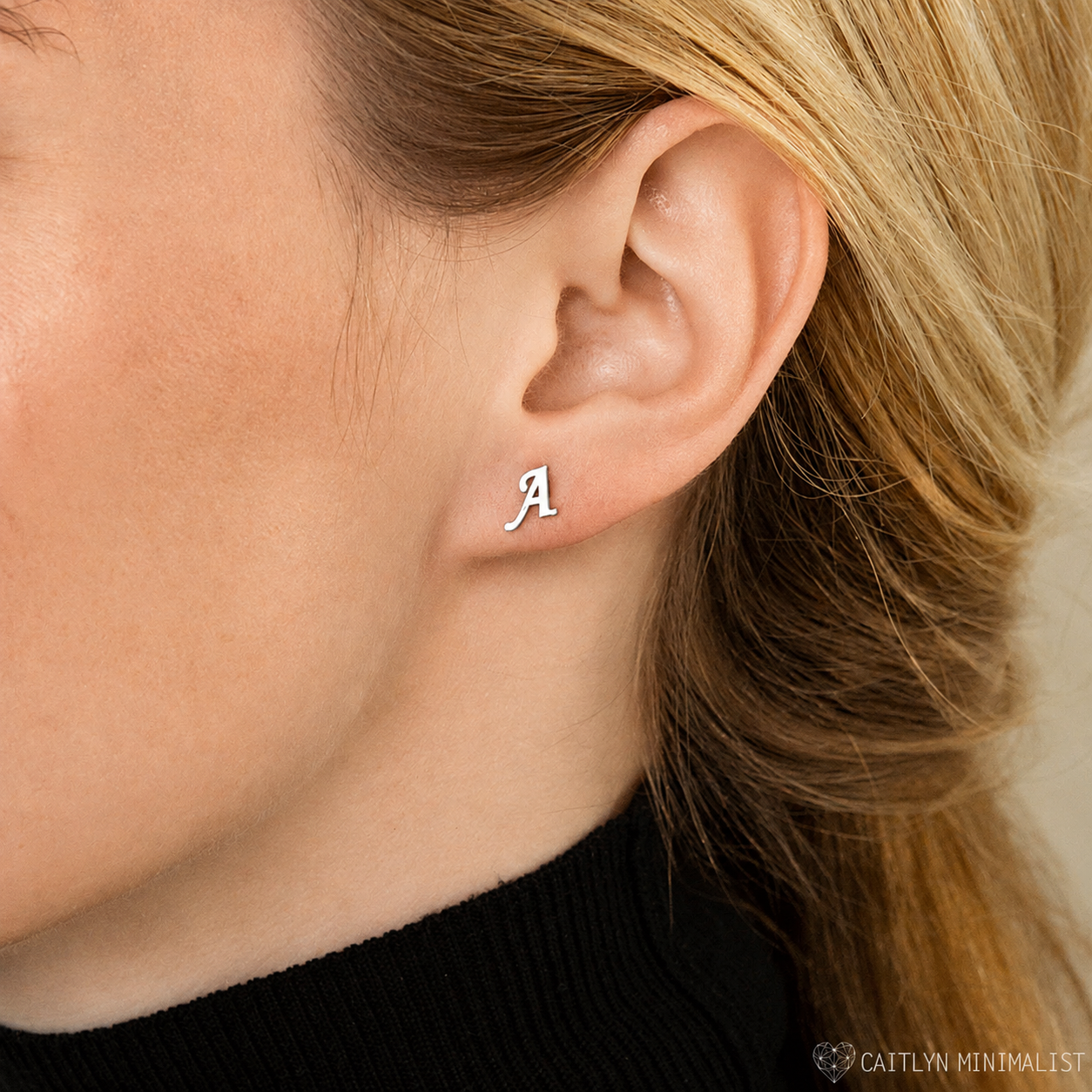 Close-up of an ear wearing a silver 'A' earring with blurred background