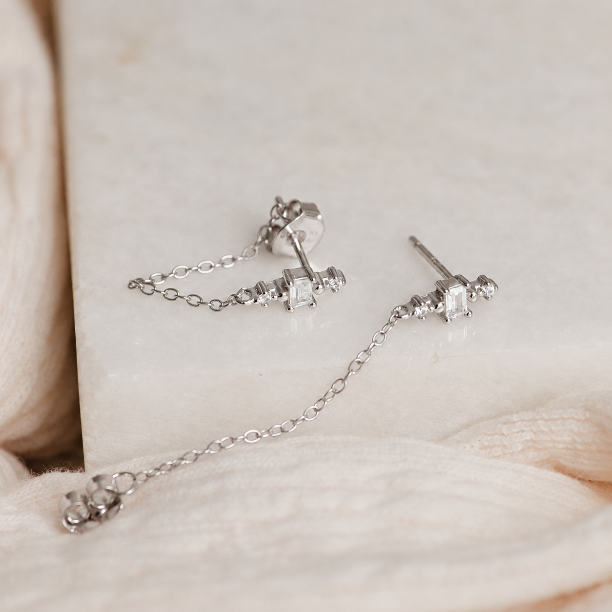 Pair of silver earrings with chain on a soft fabric background