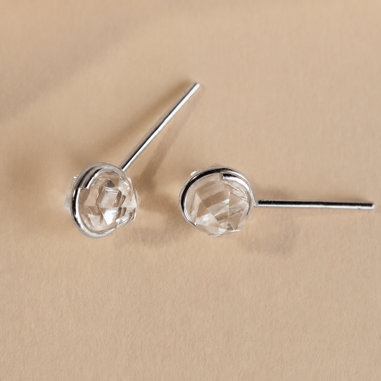 Silver earrings with clear gemstones on a beige background