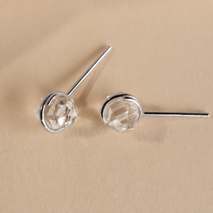 Silver earrings with clear gemstones on a beige background