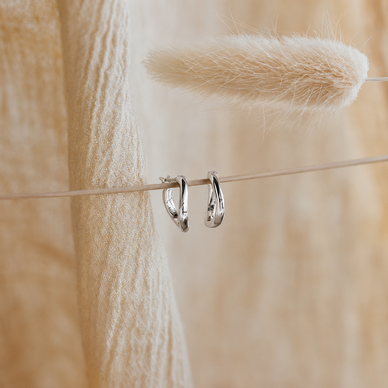 Silver hoop earrings hanging on a thin wire with a blurred natural background
