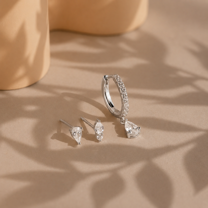 Set of silver earrings on a beige surface with leaf shadows