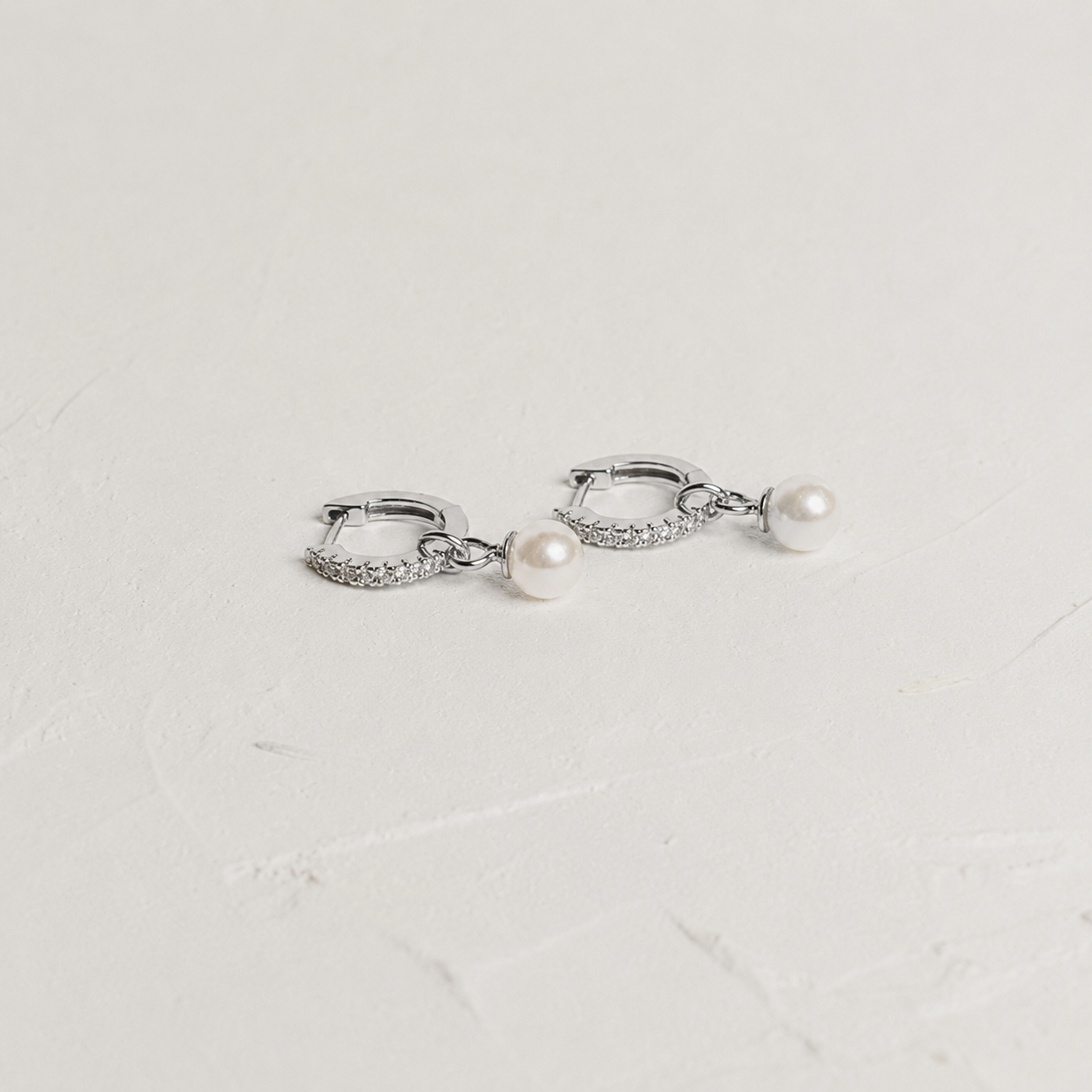 Silver hoop earrings with pearl drops on a light gray background