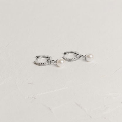 Silver hoop earrings with pearl drops on a light gray background