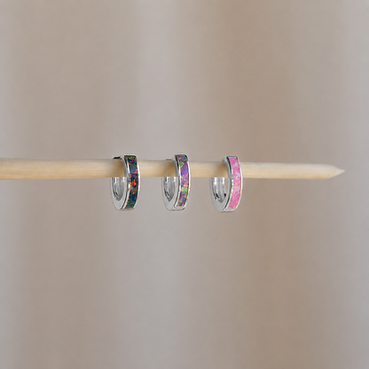 Three small hoop earrings with colorful centers on a wooden stick against a beige background