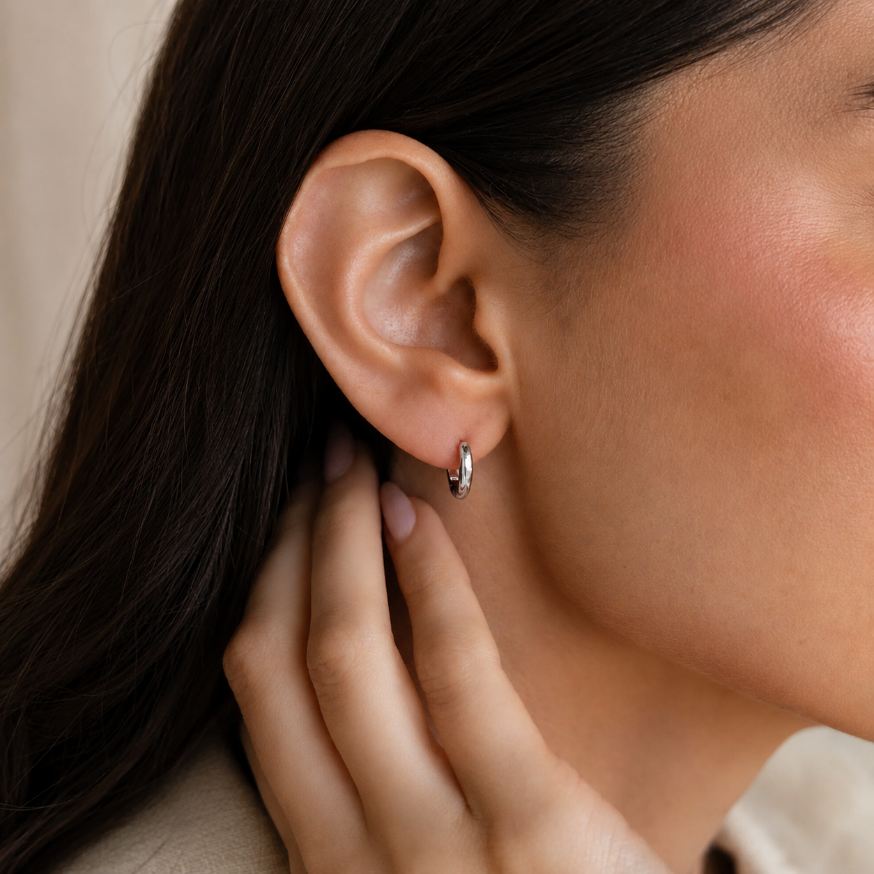 Close-up of an ear with a silver hoop earring and hand adjusting hair.