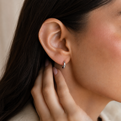 Close-up of an ear with a silver hoop earring and hand adjusting hair.