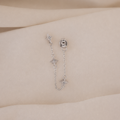 Silver chain earring with star-shaped charms on a wrist against a beige background