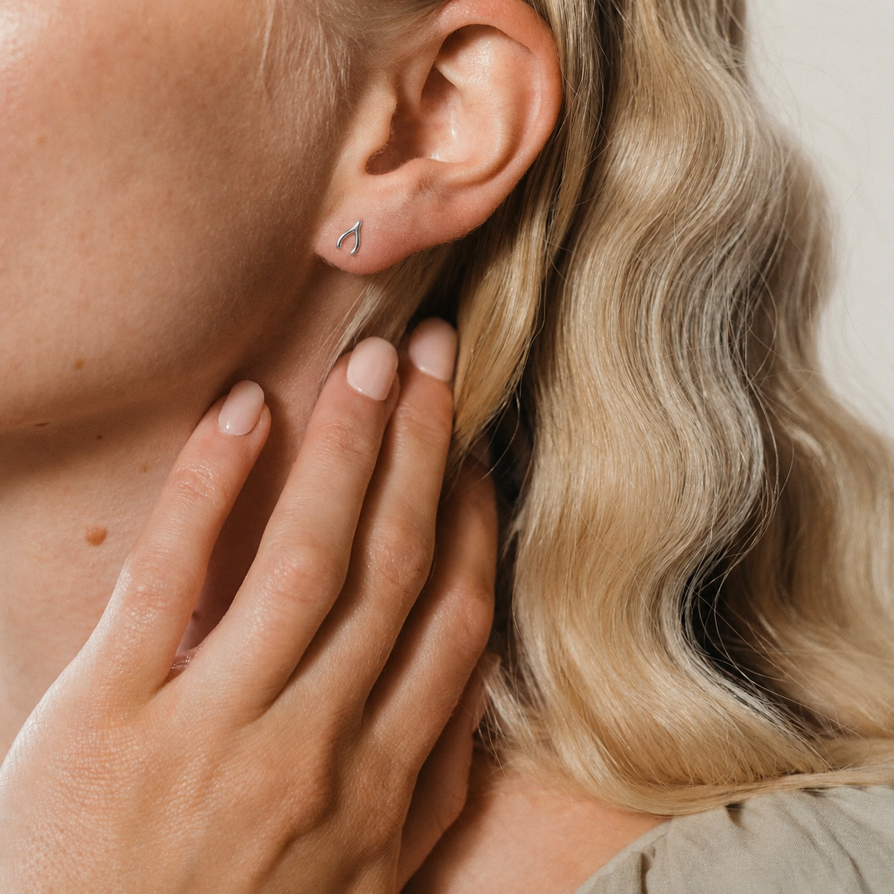 Close-up of a person wearing a small earring with a hand touching the ear.