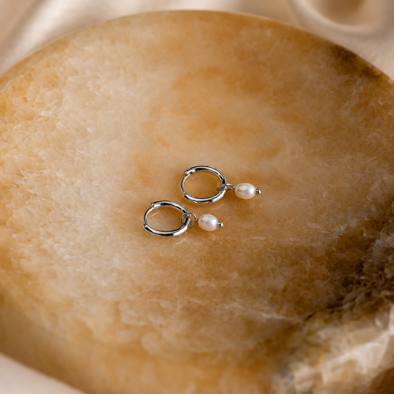 Silver hoop earrings with pearls on a textured stone surface