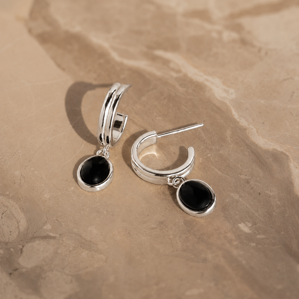 Silver earrings with black stones on a beige stone surface