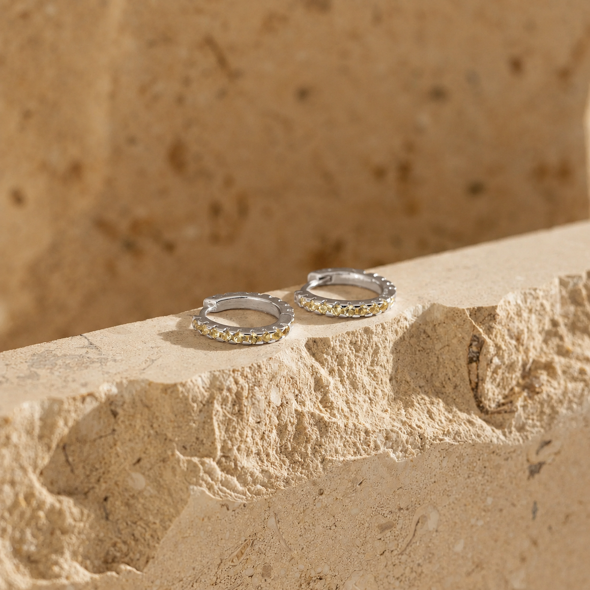 Silver hoop earrings with embedded stones on a stone surface